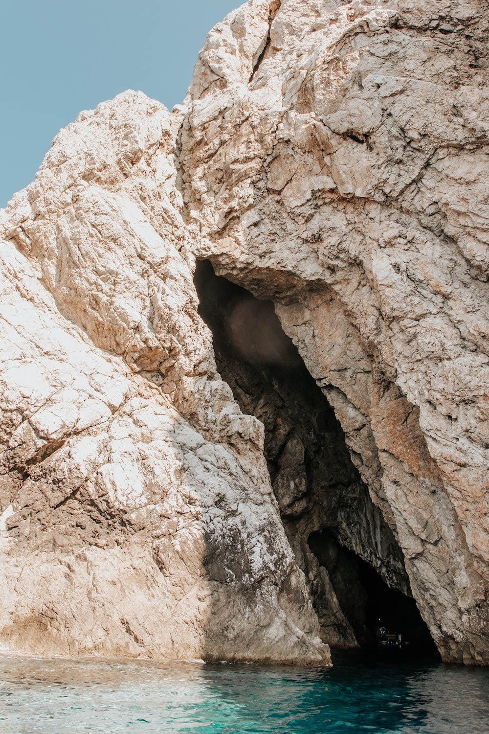 Tall cave opening in front of turquoise water - Monk Seal Cave, Croatia