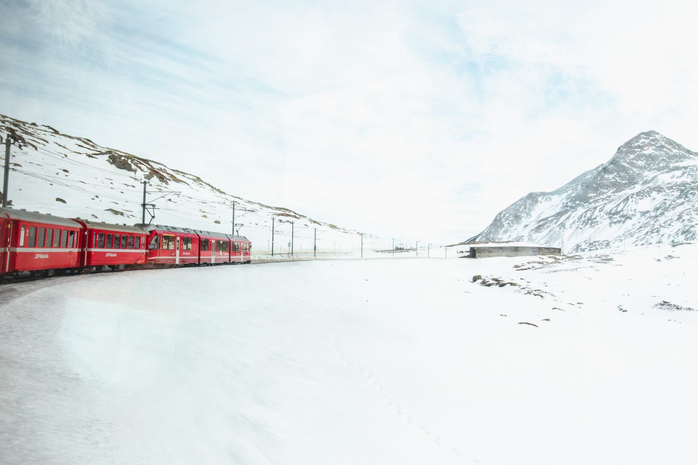 Red Bernina Express train in snowy, mountain landscape