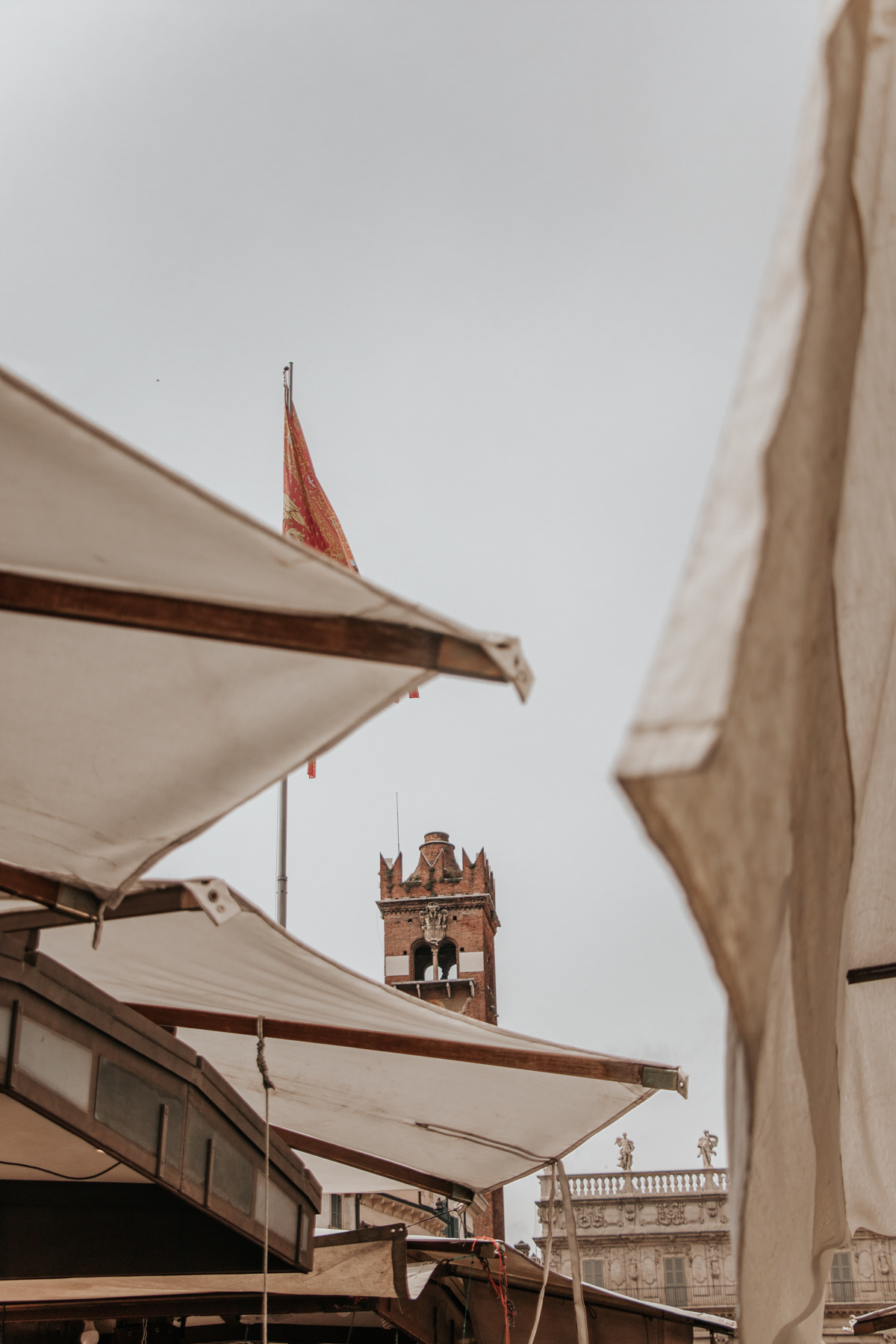 Gothic tower peeking out behind white umbrella-like roofs in Piazza delle Erbe in Verona, Italy
