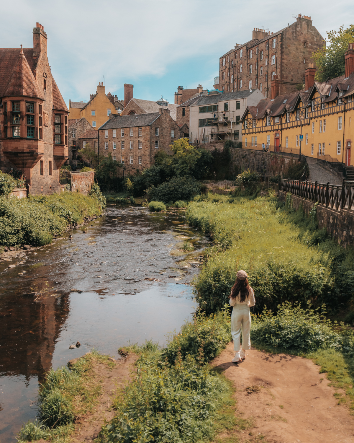 Girl standing at edge of river in front of medieval buildings - Dean Village in Edinburgh, Scotland