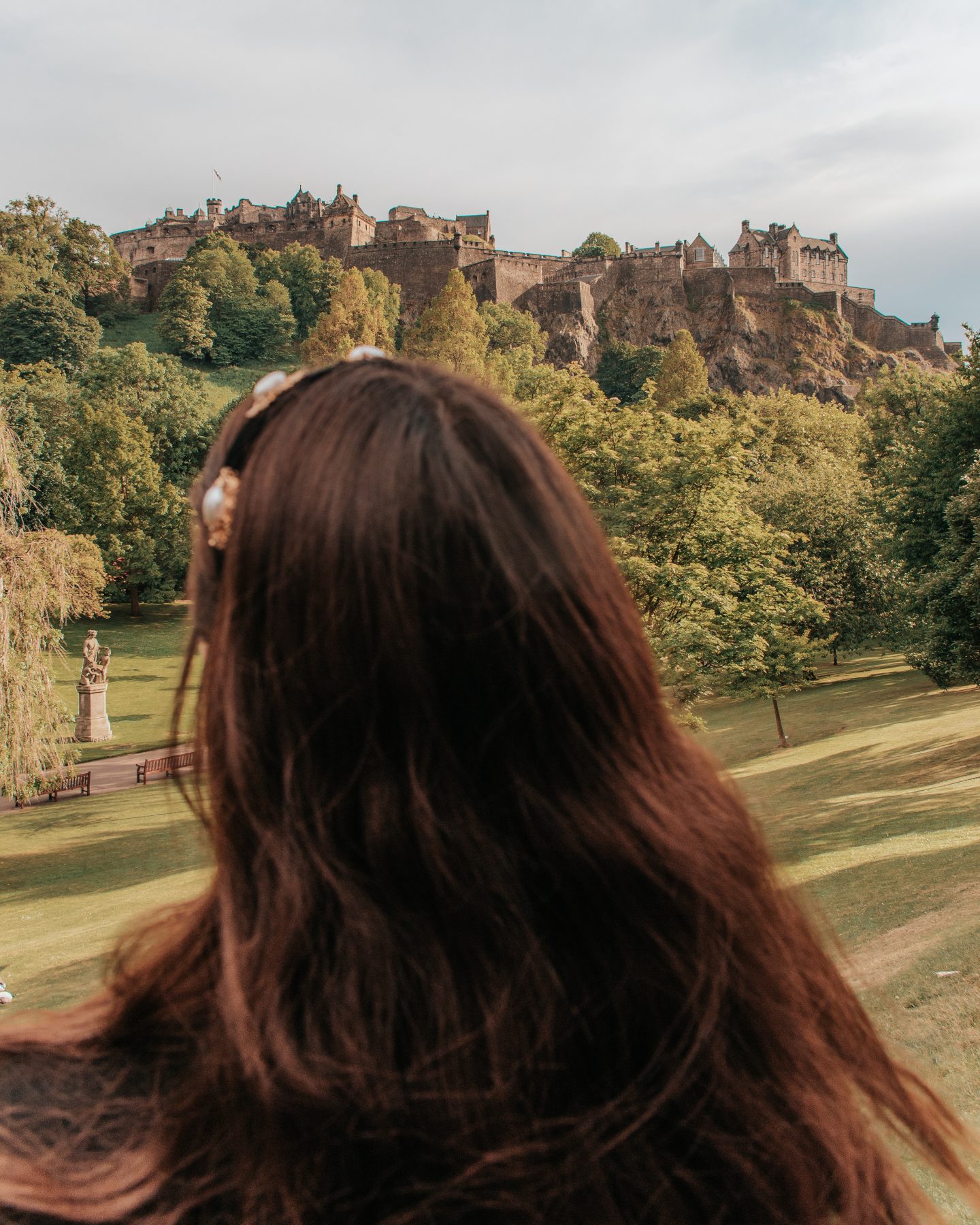 Back of girl's head in front of castle on a hill - Edinburgh Castle from Princes Street Gardens