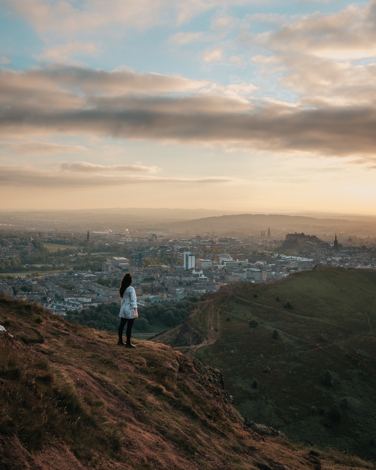 Girl standing on edge of a hill overlooking historic city, Arthur's Seat in Edinburgh, Scotland
